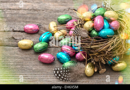 Ostereier im Nest auf hölzernen Hintergrund. Festlichen Stillleben mit mehrfarbigen Schokoladenbonbons. Stockfoto