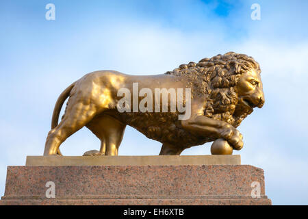 Löwe aus Bronze mit Ball, Denkmal auf Steinsockel über blauen Himmelshintergrund Stockfoto