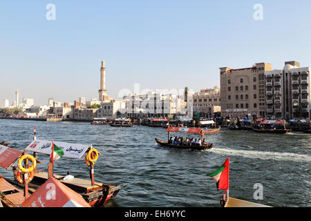 Blick über den Dubai Creek von Deira nach Bur Dubai. Abras, typische Fähren in Dubai, überqueren den Fluss; Das Minarett der G Stockfoto