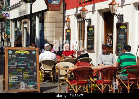 Touristen im Horseshoe Pub an der Main Street mit einer Speisekarte an Bord auf der Straße, Gibraltar, Großbritannien, Europa entspannend. Stockfoto