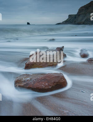 Wirbelnden Wellen mit Blick auf die schwarzen Nab Meer Stack gegen Bay, Whitby, North Yorkshire, UK Stockfoto