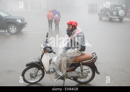 Scooter-Taxi-Fahrer raucht während er auf einen Tarif an einem nass und nebligen Tag im Stamm Hügelstadt von Sa Pa, Sapa, Vietnam wartet, Stockfoto