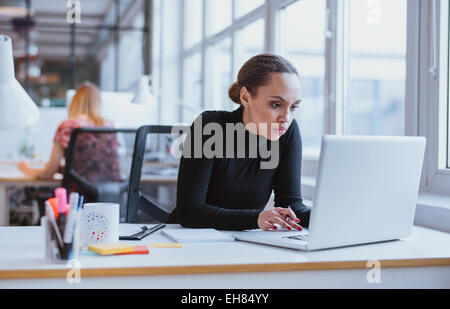 Bild der Frau mit Laptop sitzen an ihrem Schreibtisch. Junge afrikanische amerikanische Geschäftsfrau im Büro zu sitzen und arbeiten an Stockfoto