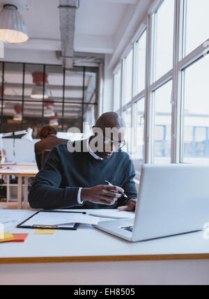 Junge afrikanische Unternehmer aufzeichnen von Notizen während der Arbeit an seinem Schreibtisch. Führungskraft im Büro arbeiten. Stockfoto