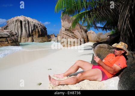 Tourist trägt einen Hut und Buch am Strand von Anse Patates, La Digue Island, La Digue und Inner Islands, Seychellen Stockfoto
