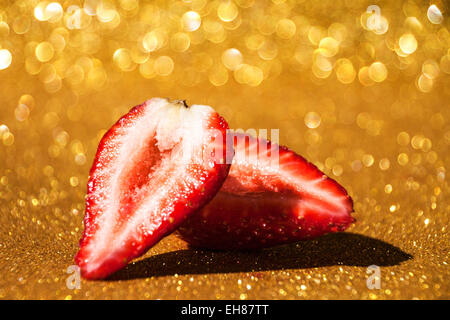 Rotgold. Eine offene Erdbeere auf einen golden glitzernden Hintergrund Bokeh. Stockfoto