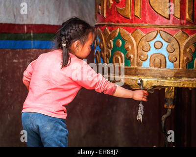 Junge Mädchen spielen mit einem großen buddhistischen Gebetsmühle in Lo Manthang, Upper Mustang, Nepal Stockfoto