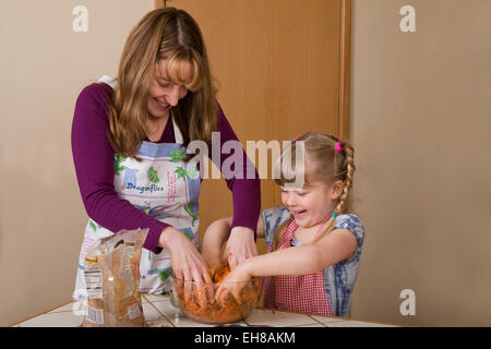 Mutter und Tochter beim Mischen, braunem Zucker und geriebene Karotten in Rührschüssel geben, bei der Herstellung Karottenkuchen lachen Stockfoto