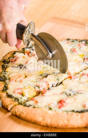 Frau mit einem Pizzaschneider, eine hausgemachte frisch gebacken, vegetarisch, Pesto, Mehrkorn, dicken Kruste Pizza zu schneiden Stockfoto