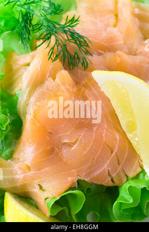 Geräucherter Lachs auf grünem Salat geschnitten. Serviert mit Zitrone und Dill. Stockfoto