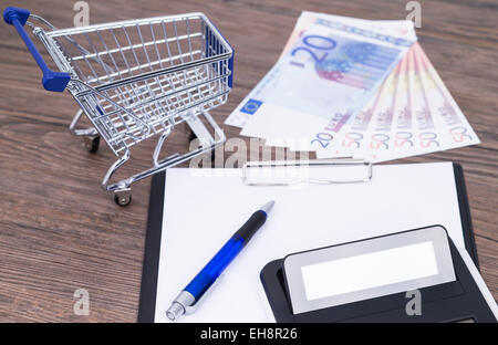 Shopping Cart, Notizblock, Geld, Rechner und Stift auf einem Holztisch Stockfoto