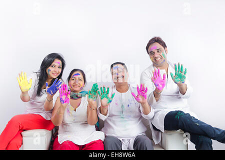 4 indische Erwachsene Eltern Sohn und Schwiegertochter Holi Festival sitzen Sofa hand zeigen Stockfoto