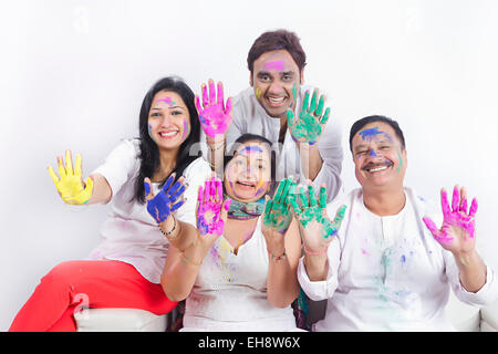 4 indische Erwachsene Eltern Sohn und Schwiegertochter Holi Festival sitzen Sofa hand zeigen Stockfoto