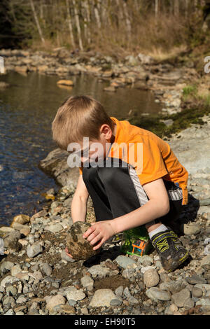 Sieben Jahre alter Junge auf der Suche nach Insekten durch Drehen über Felsen, im Olallie State Park in North Bend, Washington, USA Stockfoto