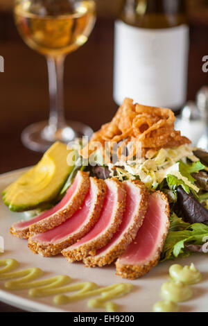 Sesam Kruste Seared Ahi mit Baby Greens, Chinakohl, Avocado, Wan-Tan-Chips, Soja Dressing Ingwer, Wasabi-Aioli und ein Glas Stockfoto