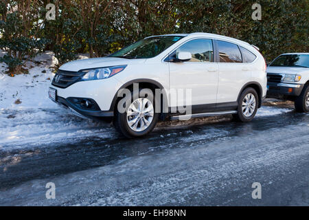 Autos auf Seite der Straße mit schwarzem Eis auf der Fahrbahn geparkt - USA Stockfoto