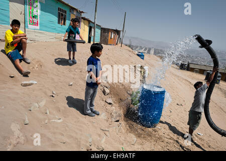 Ein peruanischer Wasser Verteilung Arbeiter mit einem Rohr spritzt Trinkwasser aus einem LKW in ein Kunststoff-Fass in Lima, Peru. Stockfoto