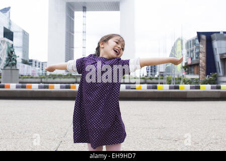 Kleine Mädchen stehen mit ihrem Kopf in den Nacken und die Arme ausgestreckt vor der Grande Arche, Paris, Frankreich Stockfoto