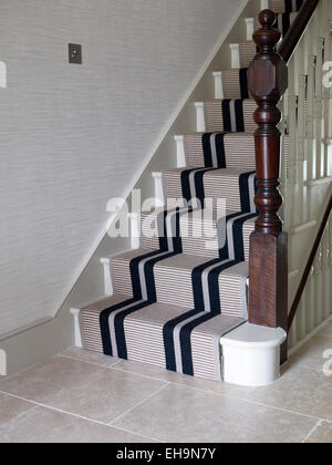 Treppe und hölzerne Balustrade mit dunklen blau gestreiften Läufer im Flur in Stevenage Road Home, UK Stockfoto