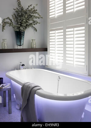 Moderne blau beleuchtete Badewanne mit Handtuch und Tisch in Fernhurst Weg nach Hause, UK Stockfoto