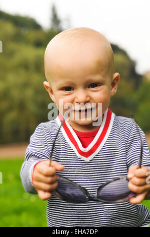 Kleine Junge Porträt Closeup lächelt und Blick in die Kamera und Sonnenbrillen zum anprobieren Stockfoto