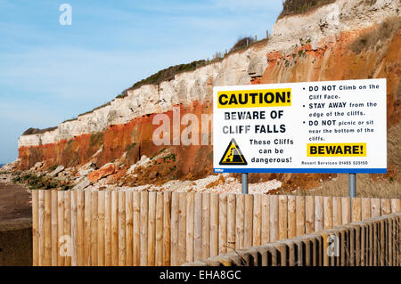 Eine Schild Warnung Klippe fällt vor den roten-weißen gebänderten Klippen von Hunstanton an der Küste von Norfolk, England. Stockfoto