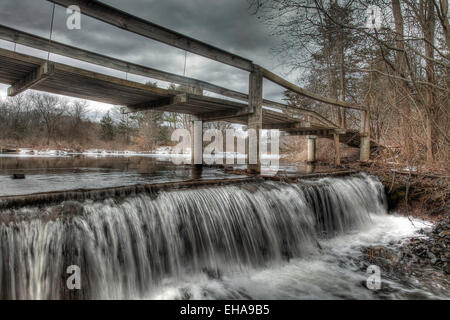 Eine alte hölzerne Fußgängerbrücke über einem Wasserfall an einem trüben Wintertag. Stockfoto