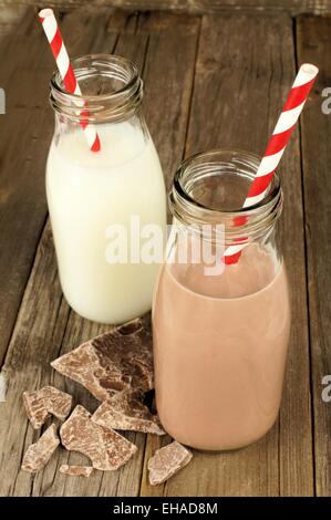 Schokolade und regelmäßige Milch in traditionellen Flaschen mit einem Strohhalm am alten Holz Hintergrund Stockfoto