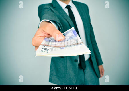 ein junger Mann im Anzug verleiht des Beobachters ein Bündel von Pfund Sterling Rechnungen Stockfoto