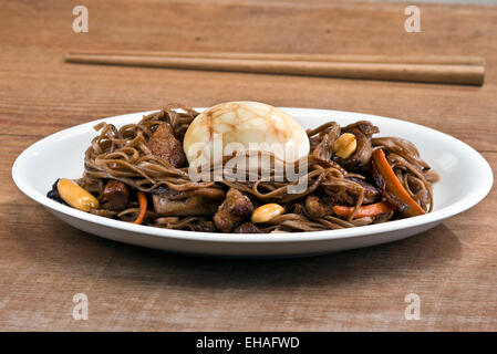 Traditionelle chinesische Tee-Ei auf ein Nest von gebratenes Soba-Nudeln mit Schweinefleisch, Austernpilze und Erdnüssen serviert. Stockfoto