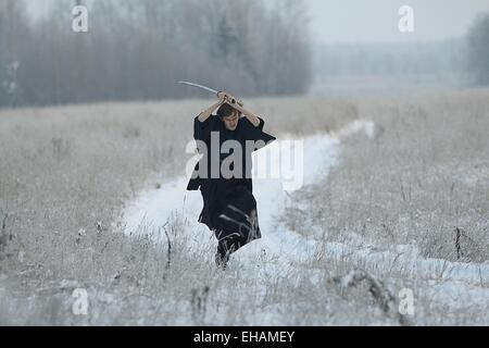 Samurai trägt einen Kimono in einem Winter Feld laufen gekleidet in schwarz, frost Stockfoto