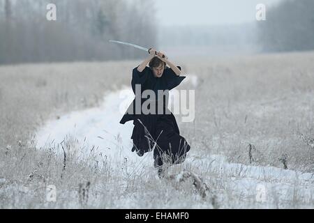 Samurai trägt einen Kimono in einem Winter Feld laufen gekleidet in schwarz, frost Stockfoto