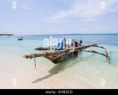 Zwei Fischer mit einem traditionellen Holzboot am Strand in Mbudya Insel in Tansania, Afrika, an einem sonnigen Tag. Horizontale. Stockfoto