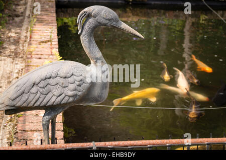 Ein wachsames künstliche Köder Reiher mit Blick auf Goldfisch in einem pool Stockfoto