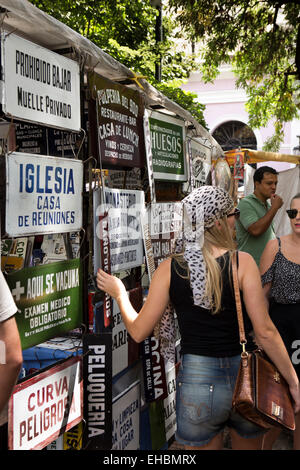 Argentinien, Buenos Aires, San Telmo Sonntag Straßenmarkt, Frau am Emaille Schild stand Stockfoto