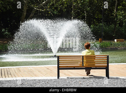 Frau ruht auf einer Bank im Park neben einem Brunnen Stockfoto