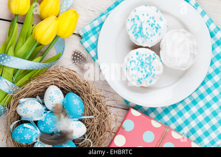 Ostern-Hintergrund mit blauen und weißen Eiern im Nest, gelbe Tulpen und traditionellen Kuchen. Ansicht von oben Stockfoto