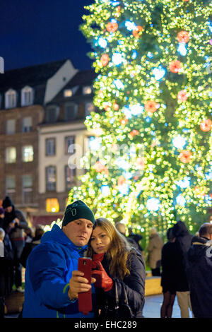 Paar unter selfie Foto vor der riesigen beleuchteten Weihnachtsbaum, der Place Kléber, Straßburg Elsass Frankreich Europa Stockfoto