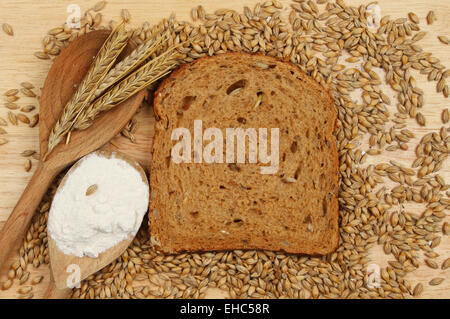 Scheibe des Multi ausgesät Schwarzbrot auf einem Holzbrett mit Gerstenkörner und Ohren von Gerste und Mehl in Holzlöffel Stockfoto