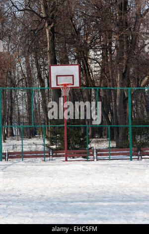 Blick auf einen öffentlichen Basketballplatz im Winter. Das Gericht ist bedeckt mit Schnee, kein Spieler nur eine einsame Rückwand Stockfoto