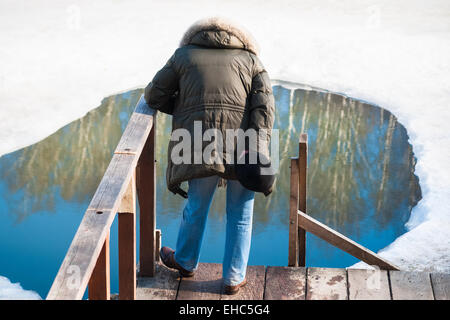 Eine nicht identifizierte, unkenntlich männliche Figur von hinten sichtbar steht auf dem Holzsteg vor dem Eisloch Stockfoto