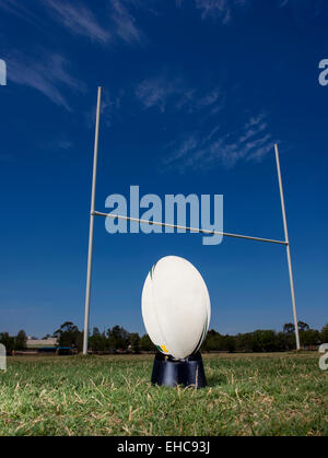Rugby-Ball sitzt auf einem munter t-Shirt, bereit, durch die Torpfosten mit blauem Himmel als Hintergrund gekickt werden. Stockfoto