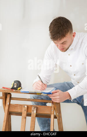 Ziemlich glücklich junger Mann arbeitet in seinem neuen Zuhause mit Ausrüstung. Stockfoto