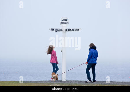 Wanderer, vorbei an dem Schild zeigt Entfernungen Endland, John O'Groats, Caithness, Schottland, mit einem Hund an der Leine Stockfoto