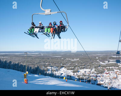 Eine Sesselbahn tragen Skifahrer auf den Berg, am Skigebiet Levi, Lappland, Finnland in der Wintersonne. Stockfoto