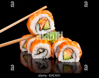 Köstliche Sushi-Rollen mit Stäbchen auf schwarzen Tisch serviert. Stockfoto