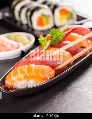 Leckere Sushi Lachs Brötchen serviert auf schwarzem Teller und Stein Stockfoto