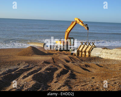 Ein Caterpillar Bagger mit Thorne Tiefbau Arbeiter hölzerne Formen von neuem Beton zu entfernen vorbereitet Buhnen gebaut am Strand von Hove, East Sussex. Stockfoto