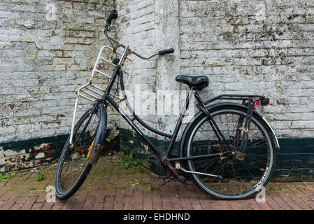 Altes schwarzes Fahrrad gegen eine schmutzige weiße Mauer. Stockfoto