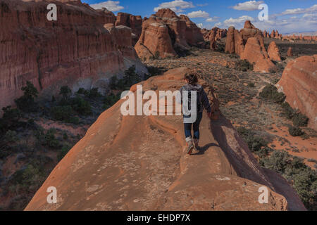 Weiblich, zu Fuß in Richtung der Kante für einen besseren Blick auf die Felsformationen in der Wüste des Arches-Nationalpark in Moab, Utah Stockfoto